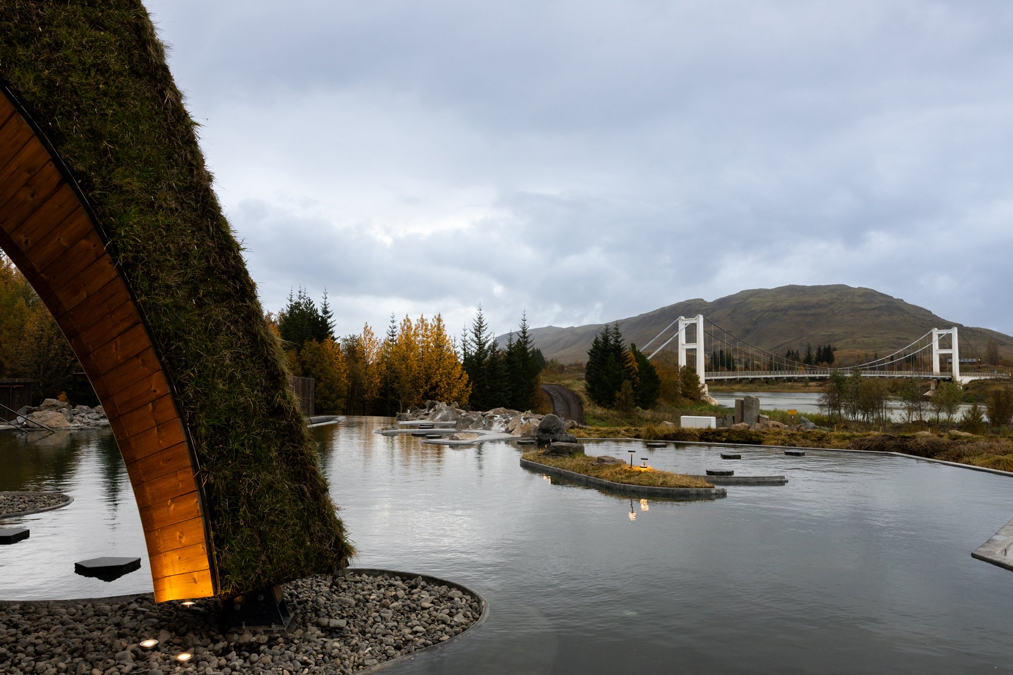 Laugarás Lagoon með mosavöxnum boga og brúnni yfir Hvítá í baksýn