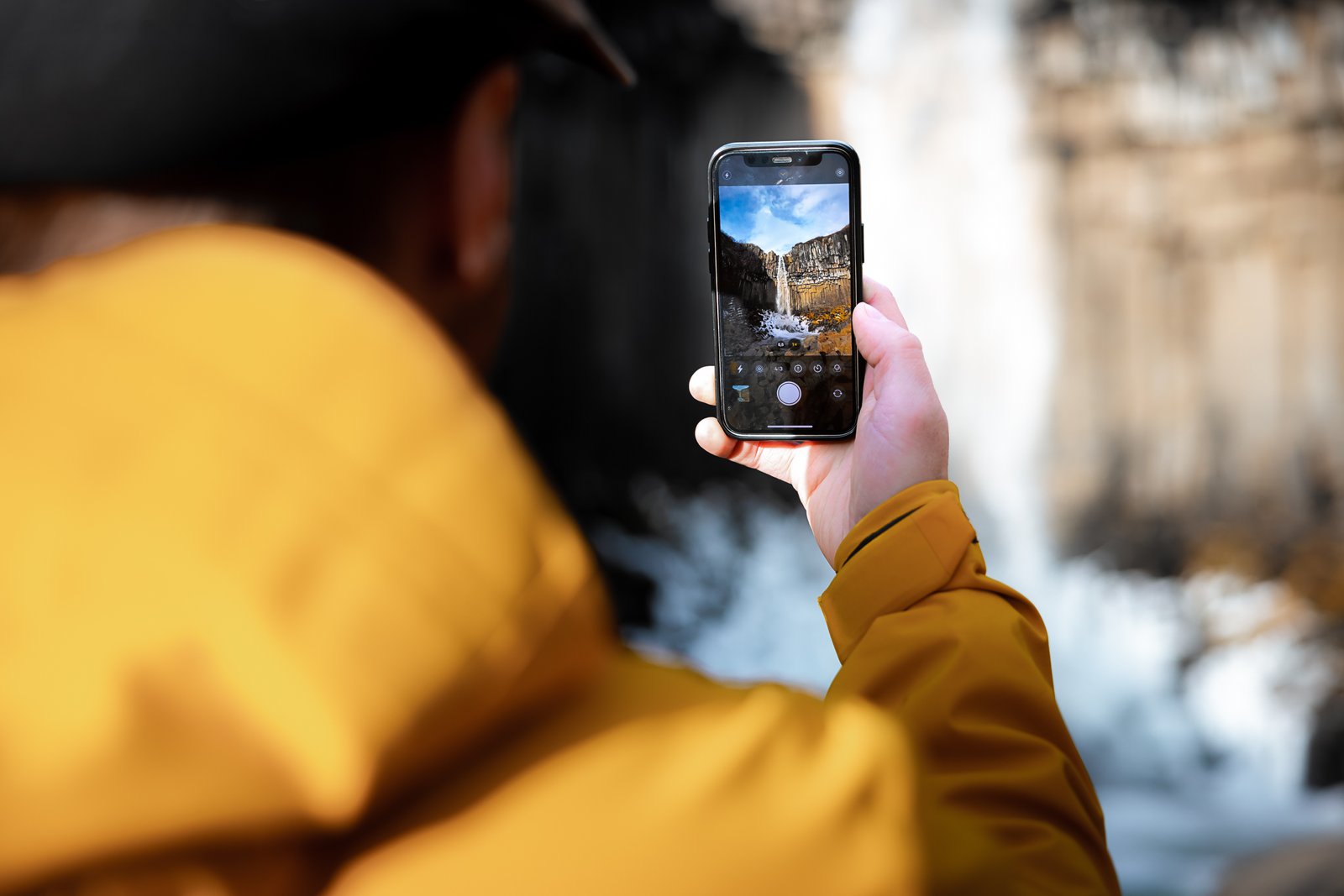 Ljósmynd: Þráinn Kolbeinsson Ljósmynd sýnir baksvip manns sem heldur á snjallsíma. Á snjallsímanum sést að maðurinn er að taka mynd af Svartafossi.